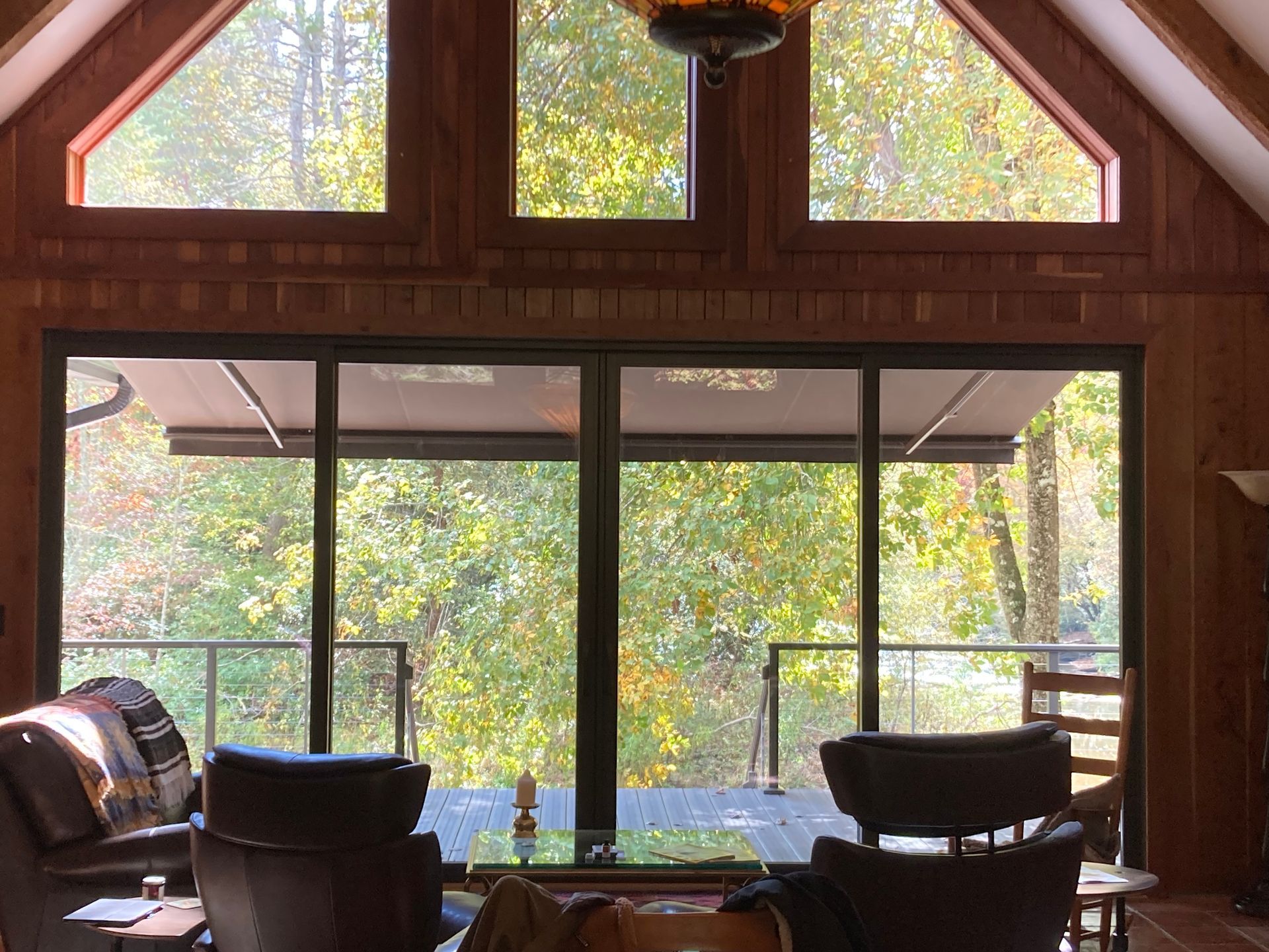 Living room with large windows overlooking a forest; two chairs, coffee table visible.
