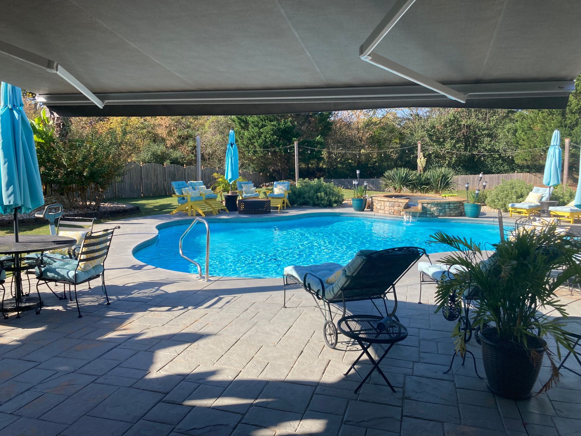 Patio with pool, blue water, and lounge chairs under a retractable awning.