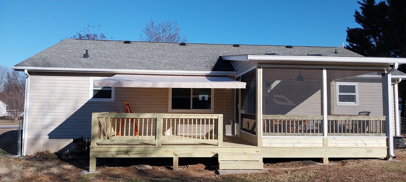 Back of a house with two decks and a screened-in porch, under a blue sky.