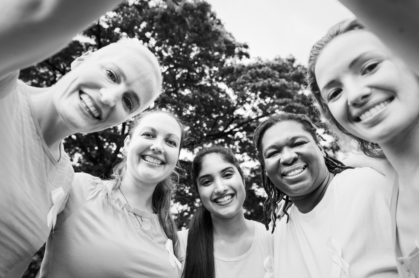 Grupo de cinco mujeres sonriendo, acurrucadas juntas al aire libre.