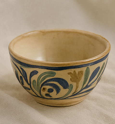 Cuenco de cerámica con diseño floral azul, verde y dorado sobre fondo beige.