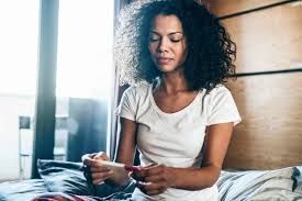A woman is sitting on a bed looking at a pregnancy test.