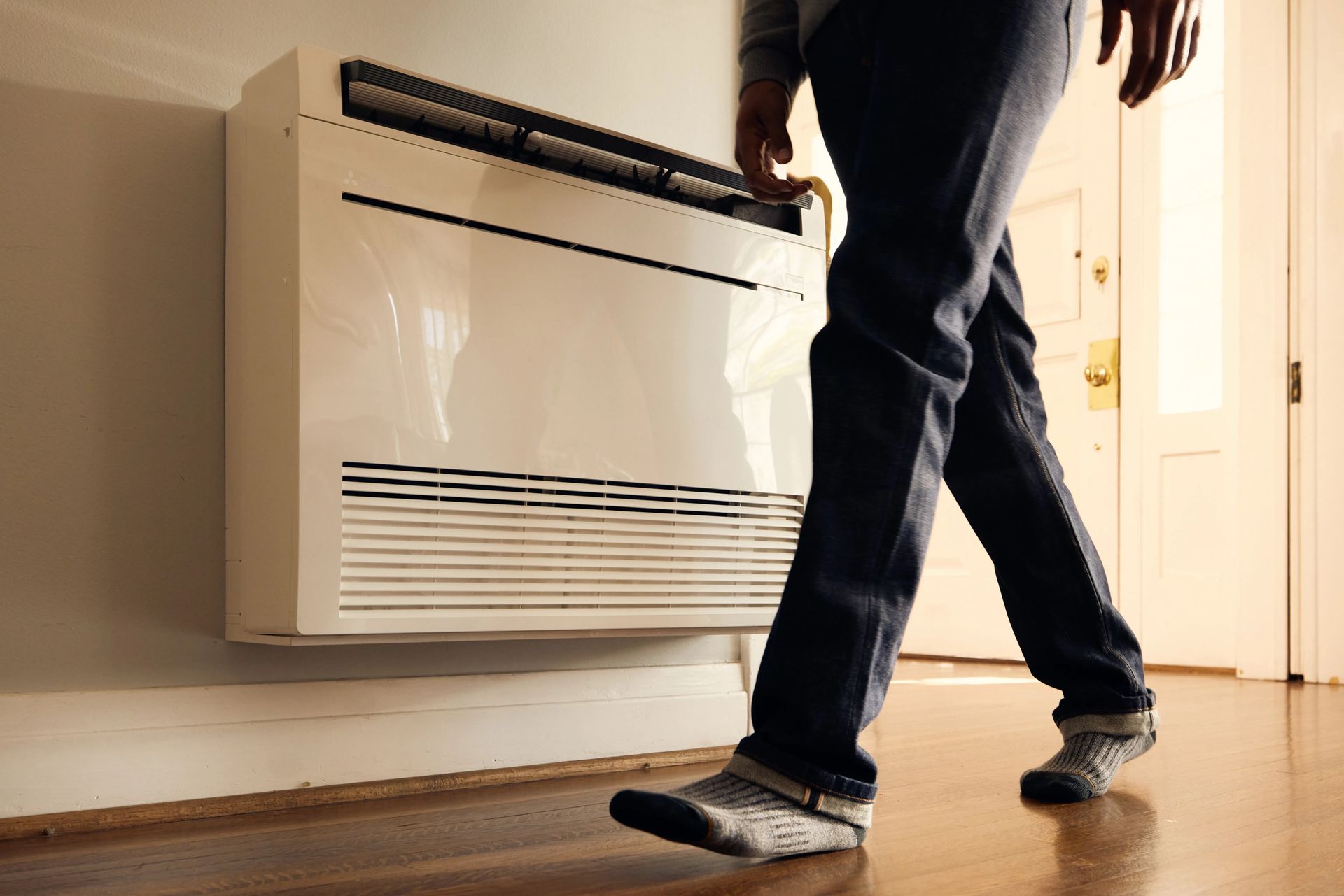 Person walking past a white wall-mounted heater in a room.