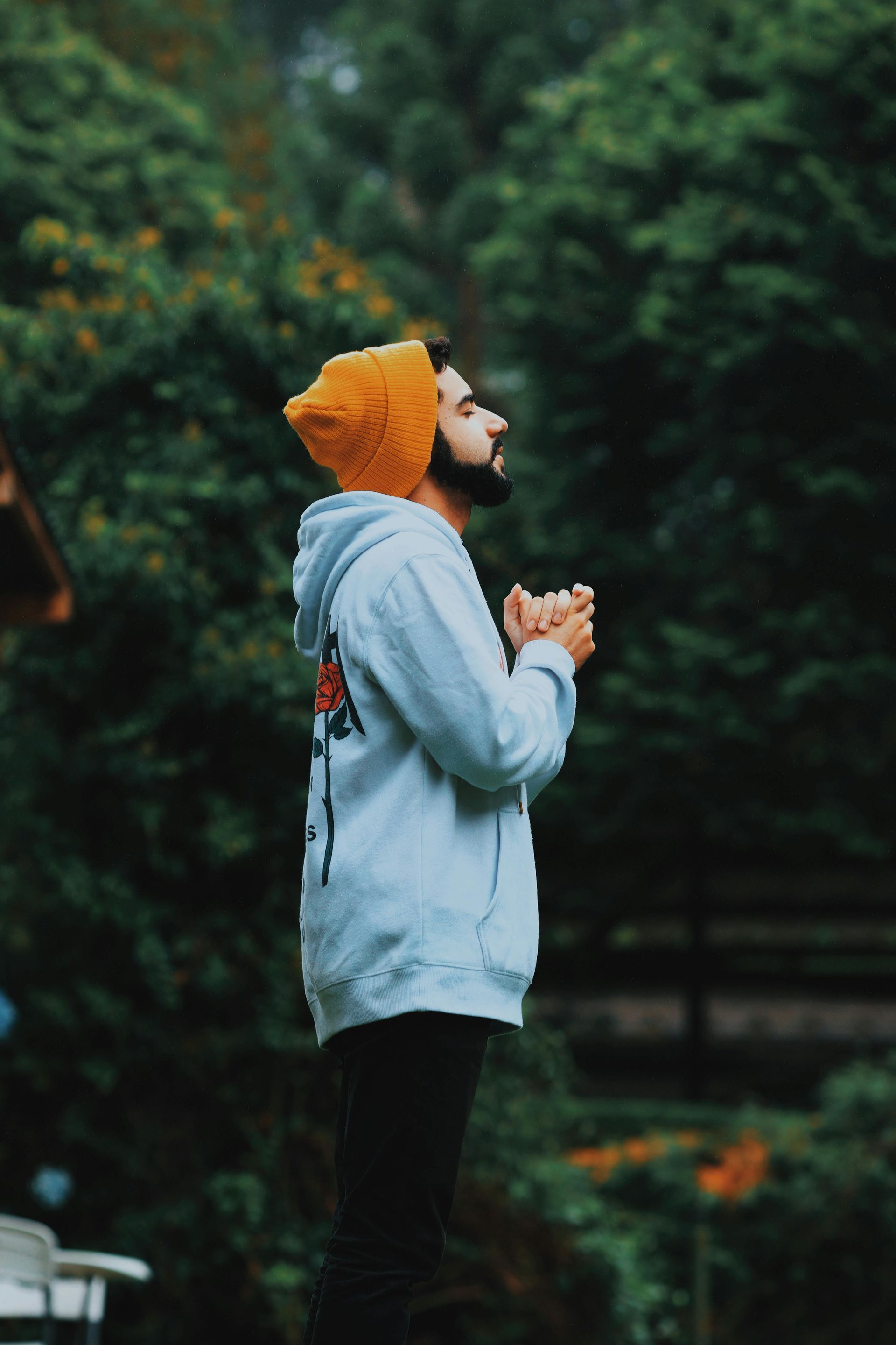A man wearing a hoodie and an orange hat is praying in the rain.