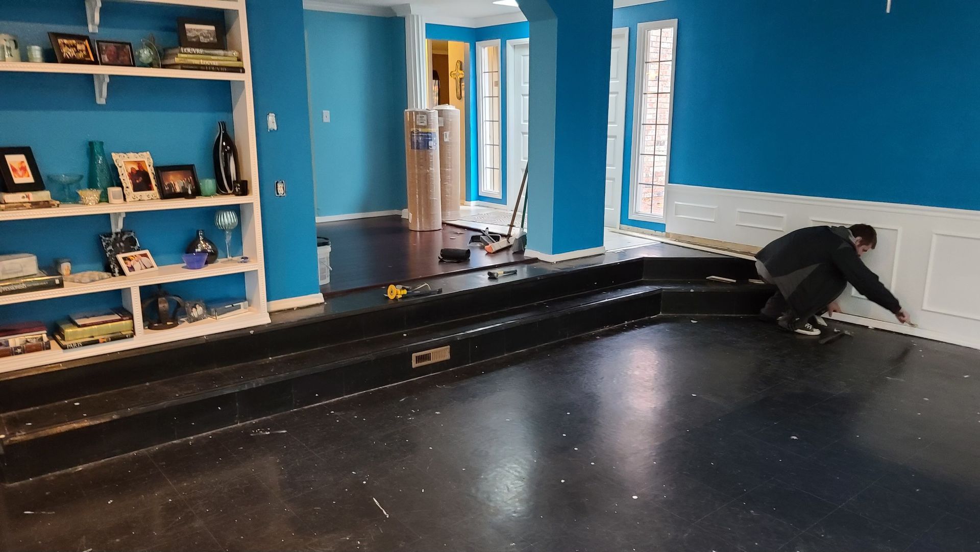 A man is kneeling on a black floor in a room with blue walls.