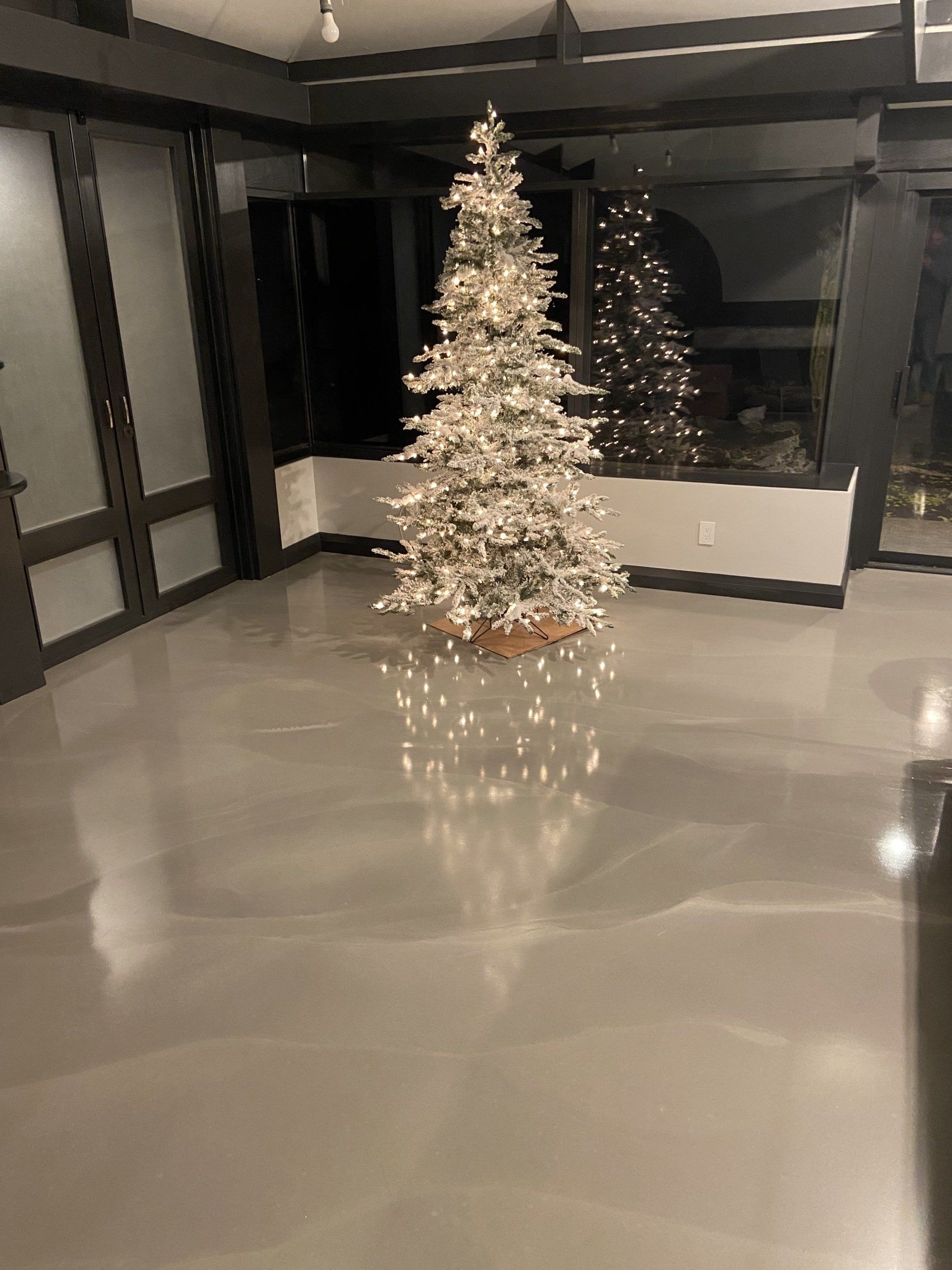 A christmas tree is sitting on a concrete floor in a living room.