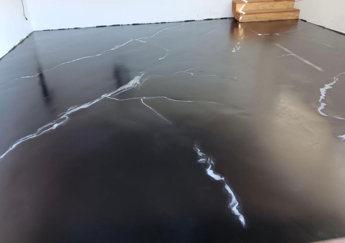 A black marble floor in a room with stairs in the background.