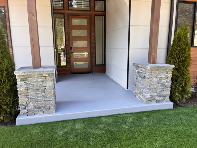 A front porch of a house with a wooden door and stone pillars.