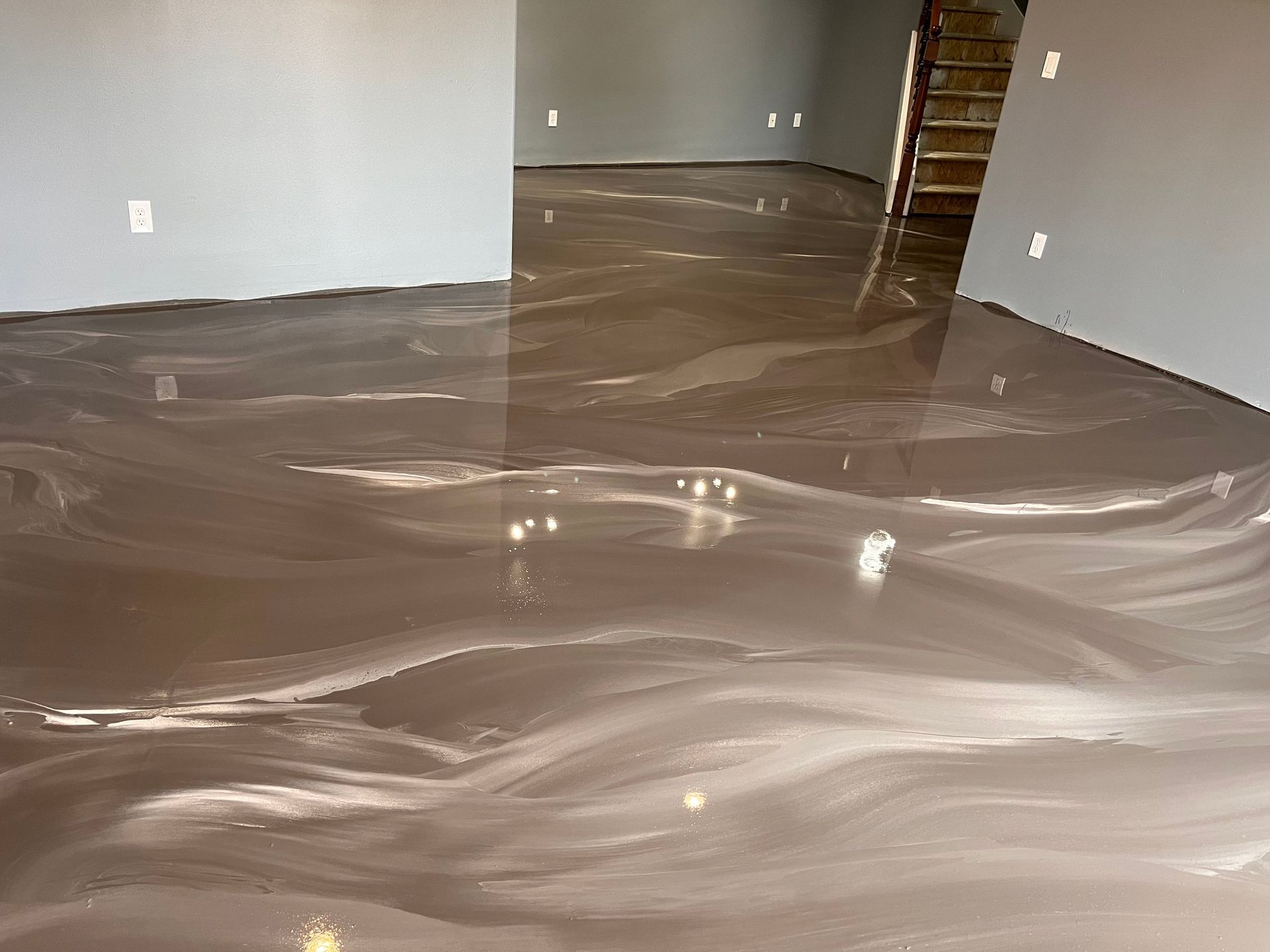 A basement with a shiny metallic floor and stairs.