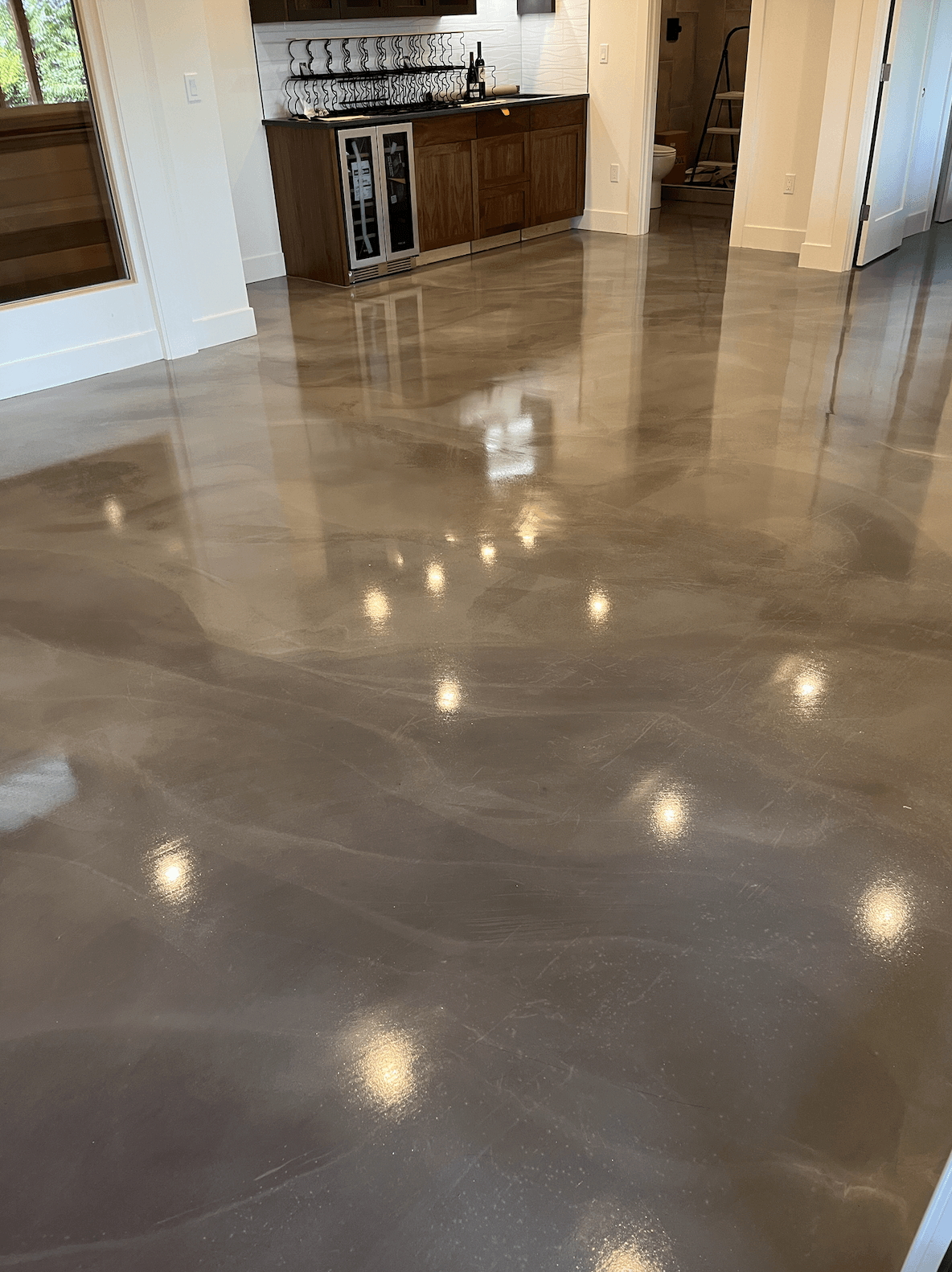 A living room with a shiny concrete floor and a kitchen in the background.