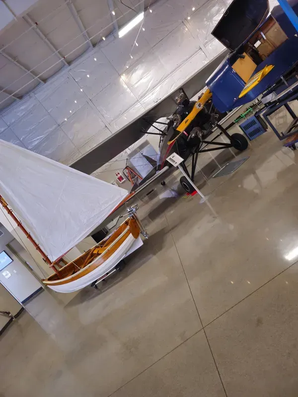 A small sailboat is sitting in a warehouse next to a plane.