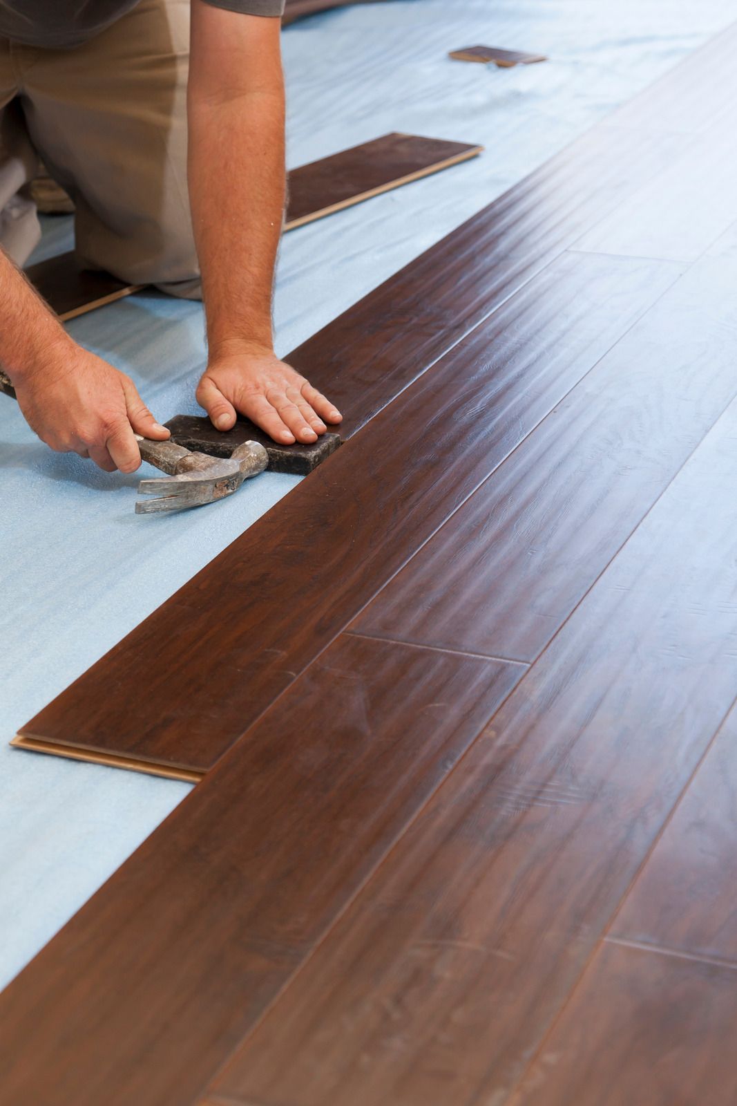 A man is installing a wooden floor with a hammer.