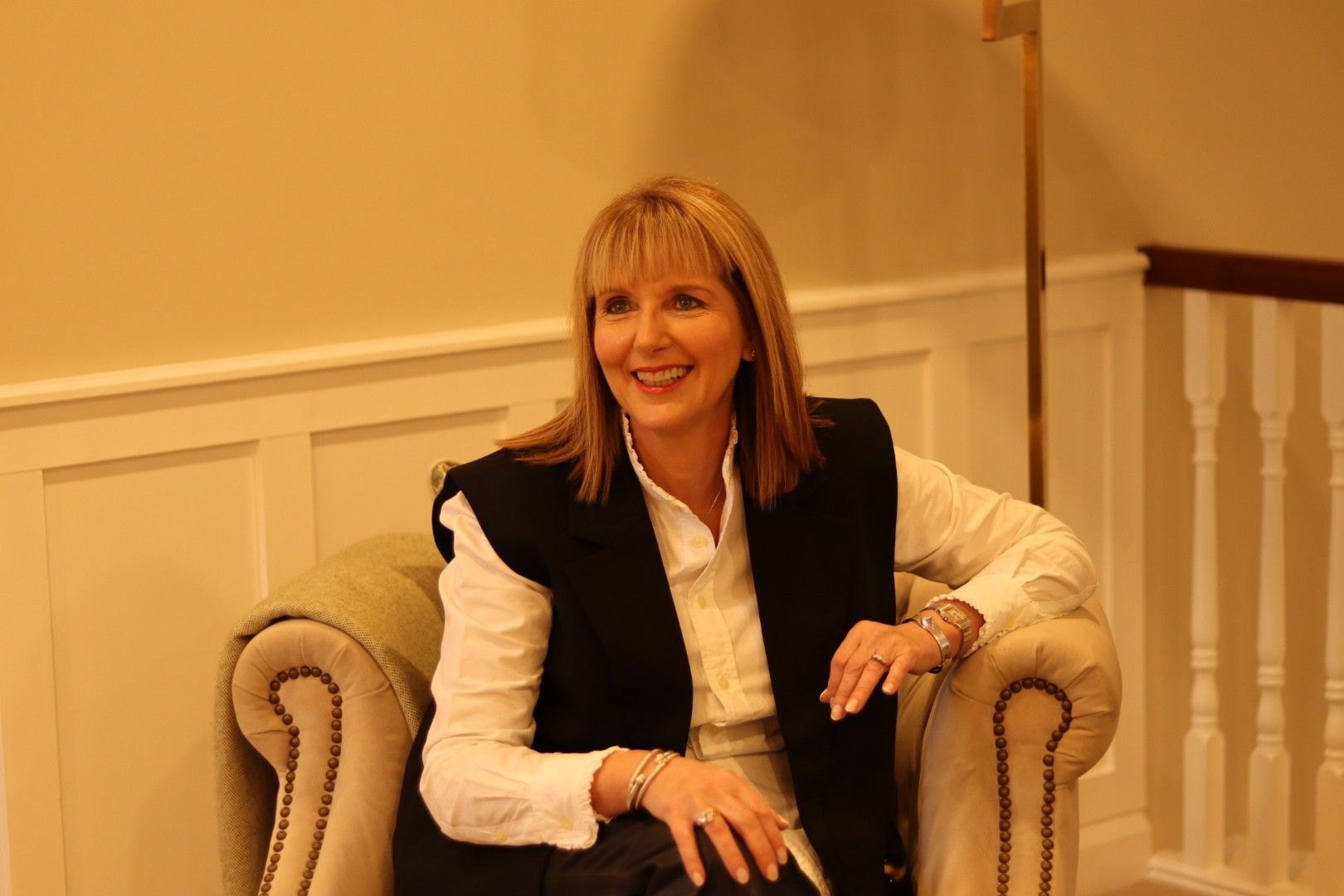 A woman is sitting in a chair with her legs crossed and smiling.