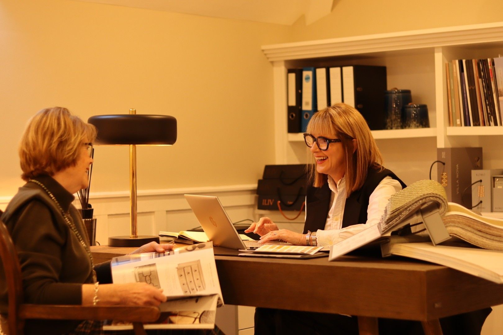 Two women are sitting at a desk with a laptop.