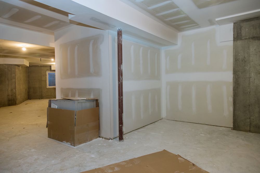 Basement under construction, drywall installed on walls and ceiling, unfinished concrete floor.