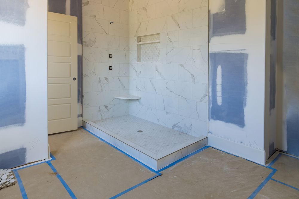 Bathroom under construction with tiled shower, built-in shelf, and blue tape on the floor. White walls, door.