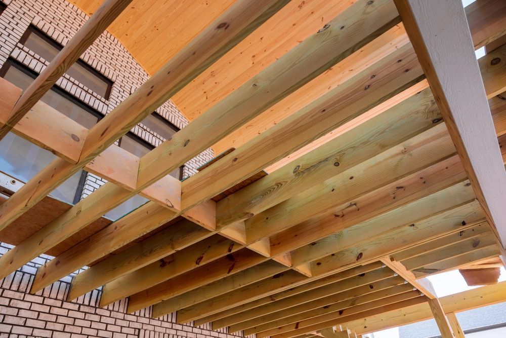 Wooden pergola structure with beams and slats, viewed from below against a brick building.