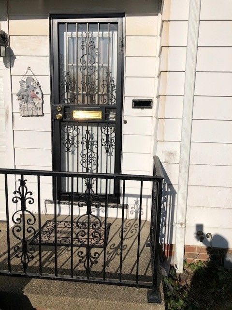 Front stoop with black iron gate, white house facade, and a decorative front door.