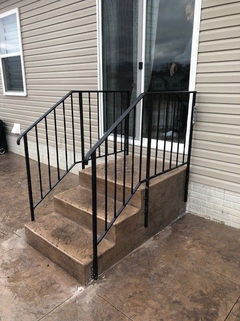 Concrete front steps with black metal railing beside a house entrance.