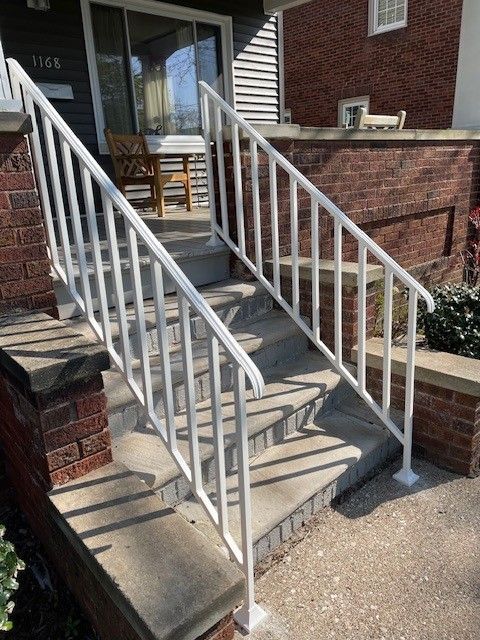 Concrete front steps with white railings leading to a porch entrance beside brick townhouses.