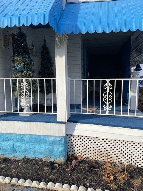Blue porch with white railings and awnings, decorated for the holidays with a lit Christmas tree.