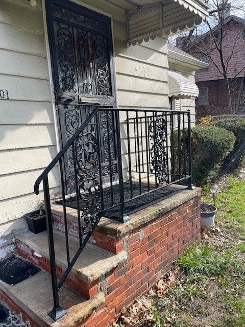 Front porch with brick steps, black railing, and a decorative metal security door on a house
