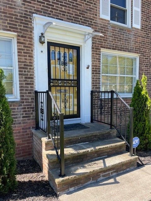 Front entrance of a brick house with stone steps, black metal railings, and a white-framed door with a security gate