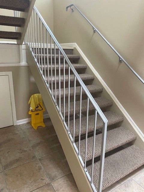 Indoor stairway with beige carpeted steps, white railing, and yellow wet floor sign on the landing