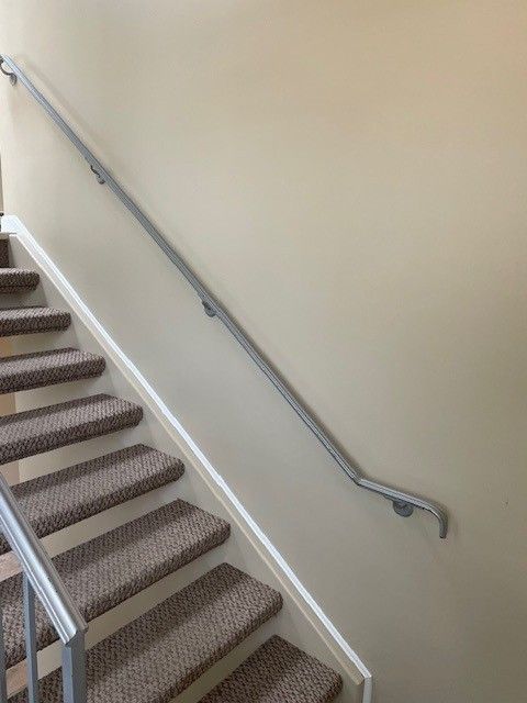 Stairwell with carpeted steps and a metal handrail along a beige wall