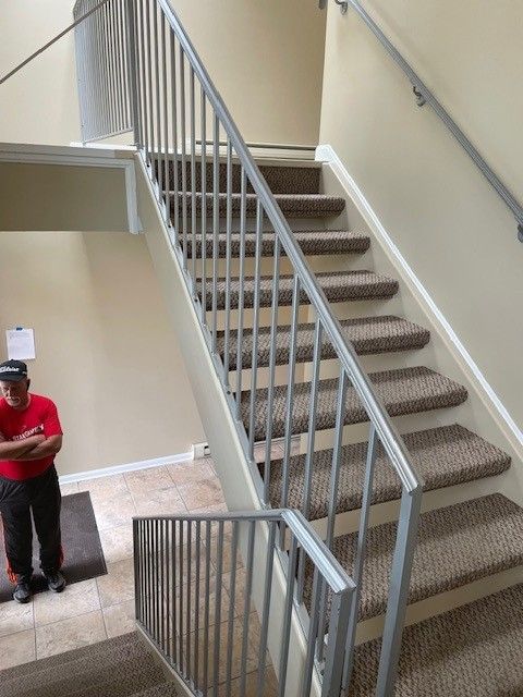 Carpeted indoor stairwell with white railings and a person standing at the bottom left.