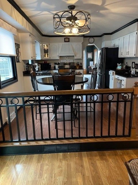 Open kitchen with white cabinets, black accents, hardwood floor, and a decorative railing in the foreground