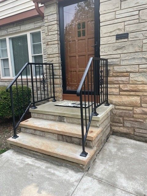 Front steps with black railings leading to a wooden front door on a stone house.