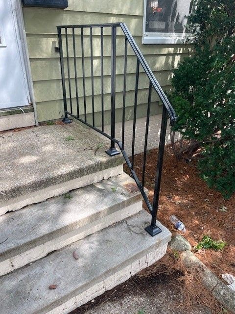 Black metal railing beside concrete steps leading to a house entrance