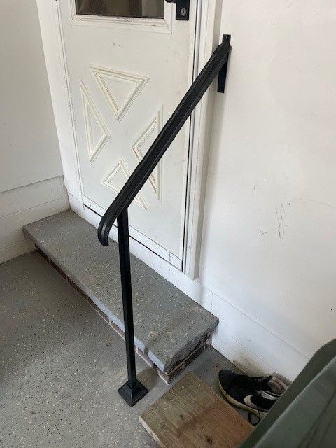 Black handrail beside a small step at a white door entrance