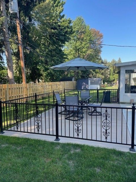 Backyard patio with black metal fence, umbrella table, and lawn beside a small shed