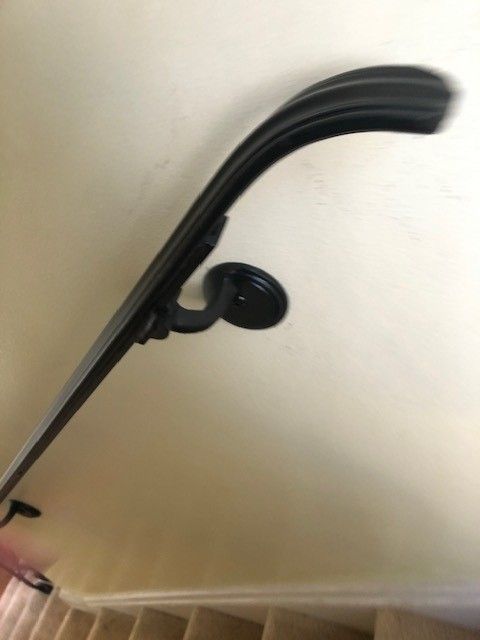Black curved handrail mounted on a light-colored wall, viewed at an angle.