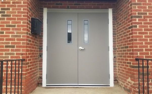 Closed gray double doors in a brick building entrance with narrow windows