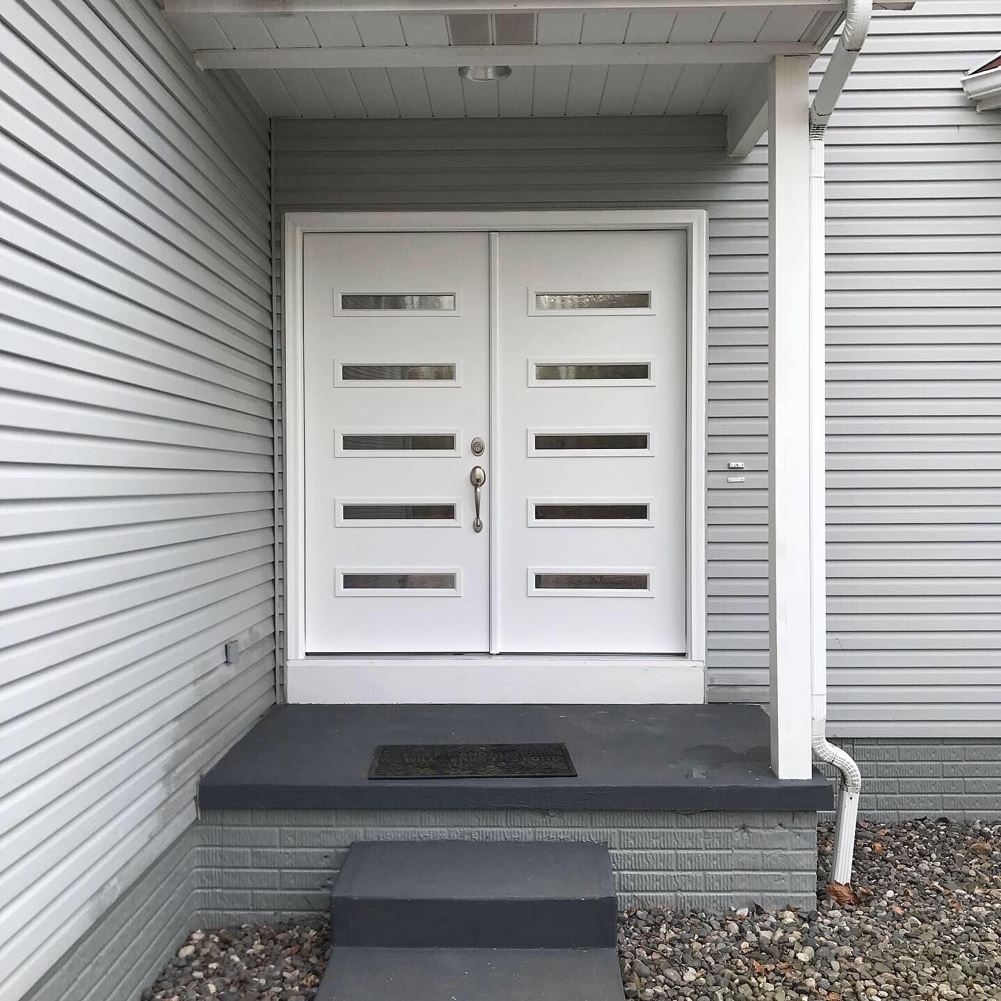 White double front doors with five horizontal glass panes each, set in a light grey home entry with a small concrete step. White double front doors with five horizontal glass panes each, set in a light grey home entry with a small concrete step.