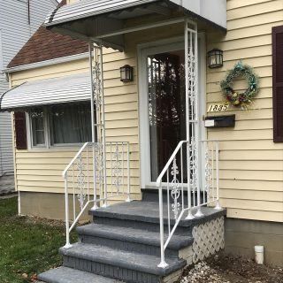 Front porch entrance with gray steps, white railings, beige siding, and a wreath by the door.