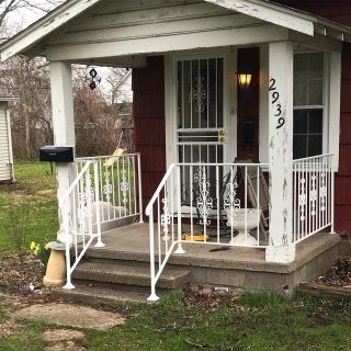 Small front porch of a house with white railings, a red door, and house number 2939.