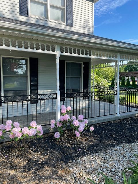 Front porch with white siding, black railing, and pink flowers in a garden bed