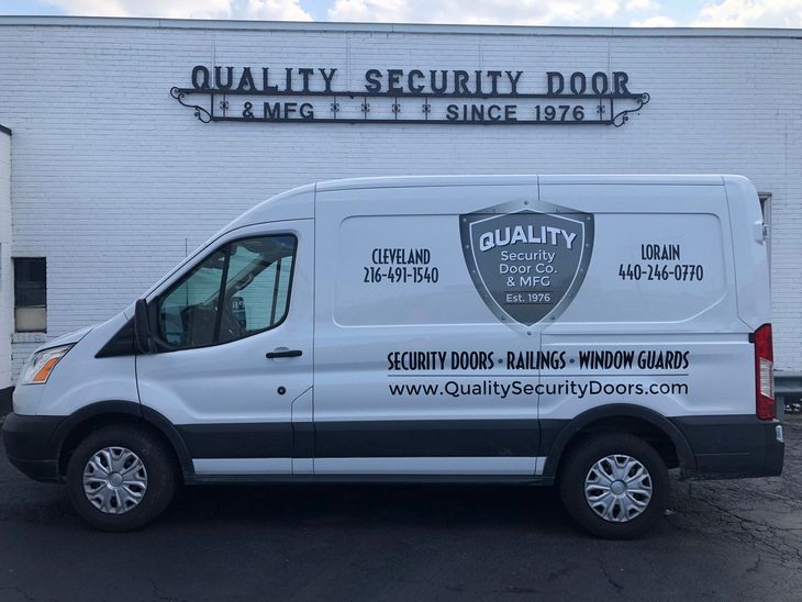 A white work van parked in front of a building with Quality Security Door & Mfg signage.