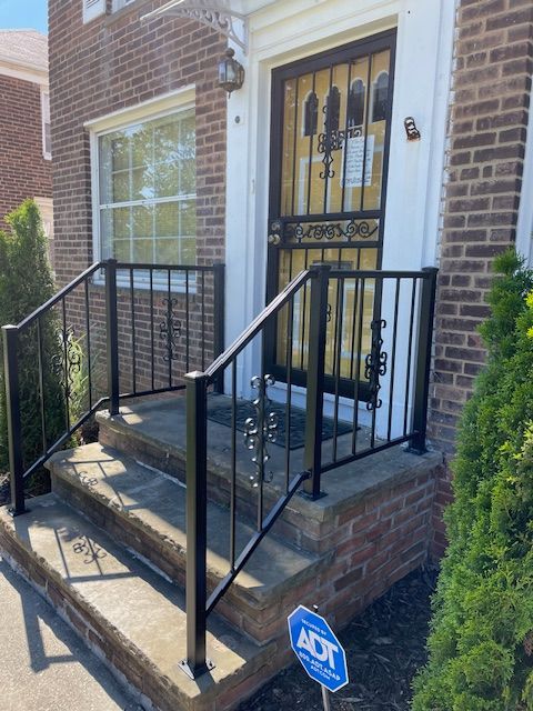 Front steps of a brick townhouse with black railings and a decorative metal front door.