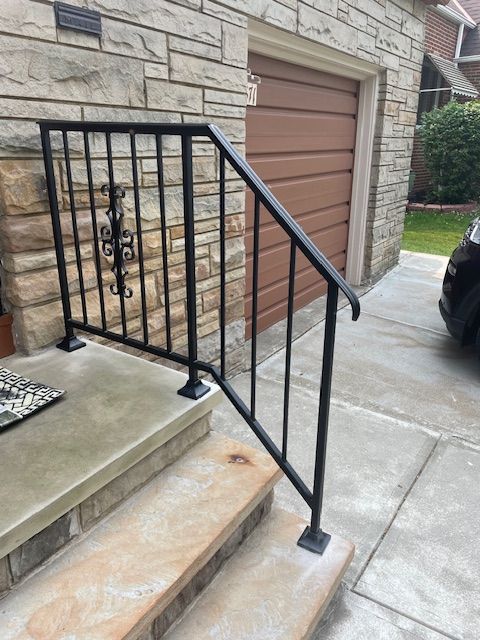 Exterior concrete steps with black metal railing beside a stone garage and driveway