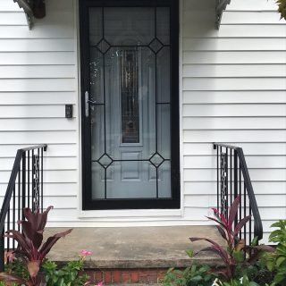 Front porch with black-framed glass door, white siding, and potted plants by the steps