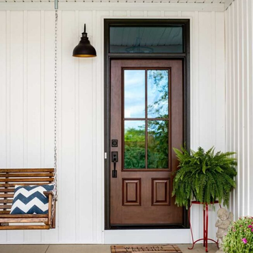 Front porch with brown door, black lantern, wicker swing, and potted fern against white siding