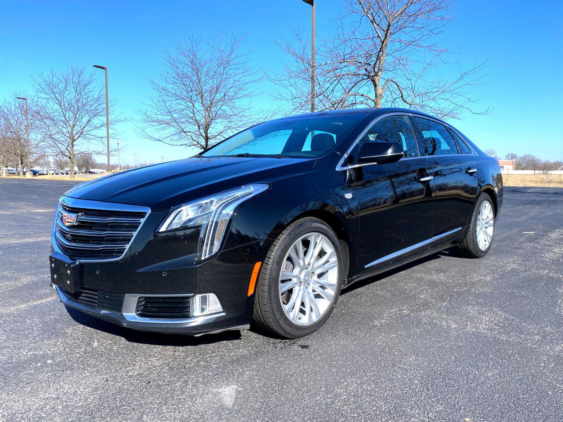 Black Cadillac XTS sedan parked outdoors on a sunny day, with bare trees in the background.