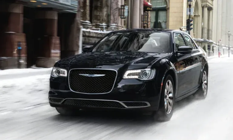 Black Chrysler 300 sedan driving on a snowy city street, moving from the viewer's perspective.