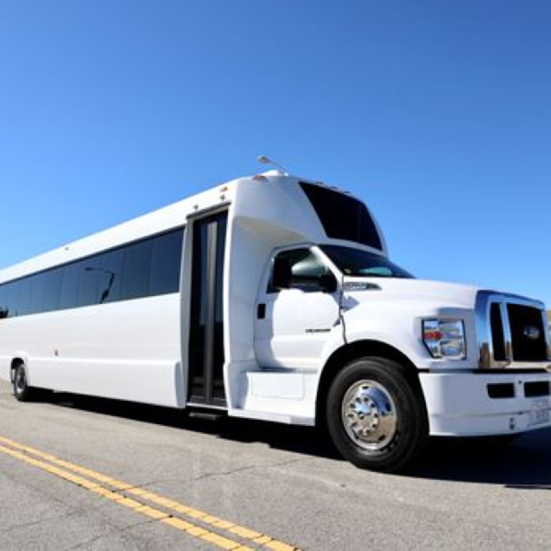 A white party bus parked on a sunny street, with its door open against a clear blue sky.