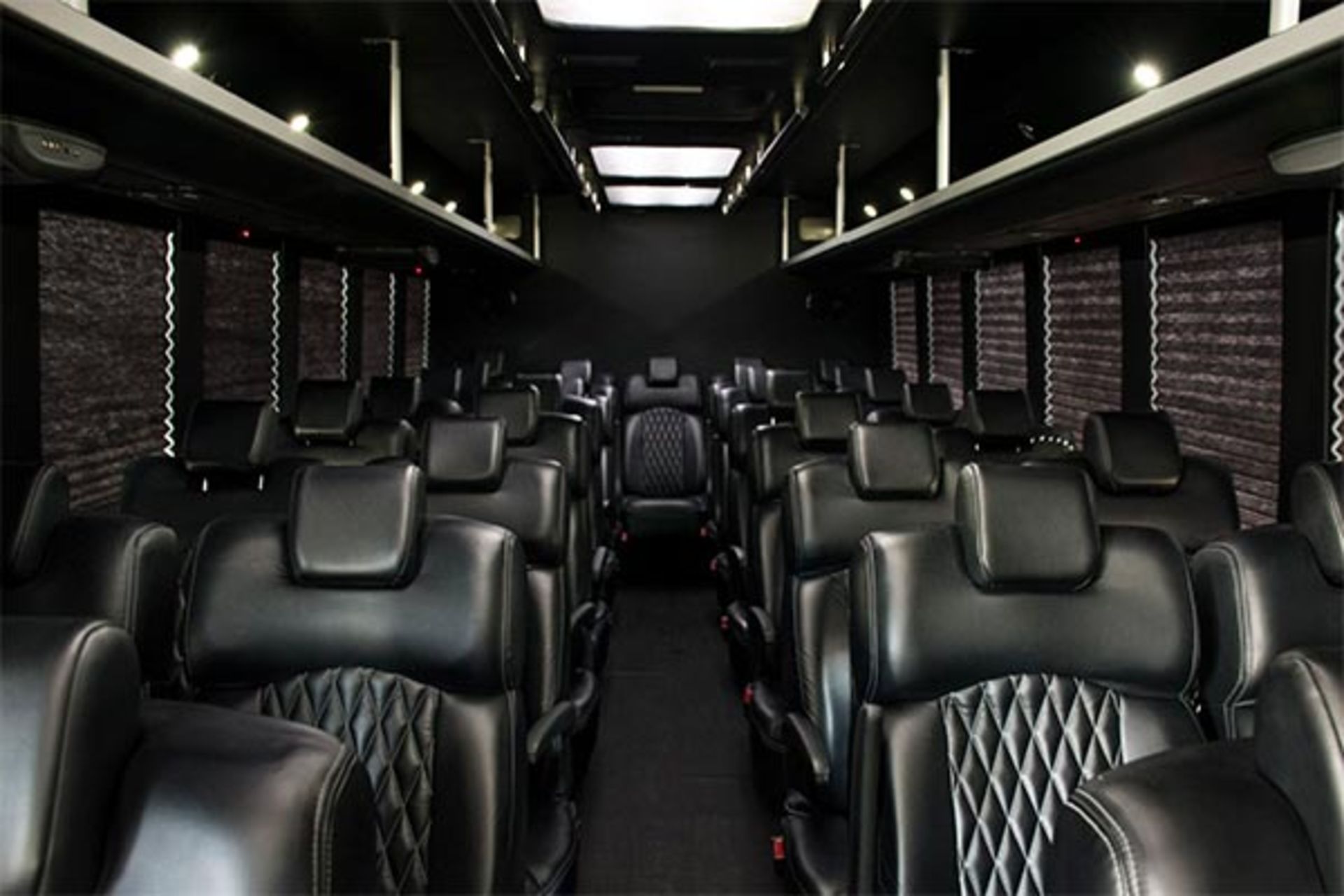 Interior of a black bus with rows of black leather seats, black walls and shades, and a center aisle.